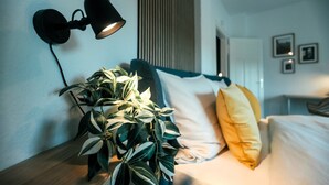 A neatly arranged bedroom with a bed, a bedside lamp, and a potted plant.
