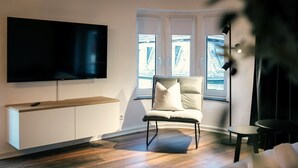 A modern living room with a flat-screen TV mounted on the wall, a comfortable chair, a small round table, and a sofa.