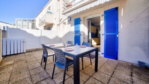 Un patio al aire libre con una mesa, sillas, una pared blanca y contraventanas azules.