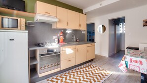 Cocina moderna con microondas, estufa y lavamanos. Hay un refrigerador pequeño y un microondas en la encimera. La cocina tiene armarios de madera y una campana extractora de acero inoxidable.