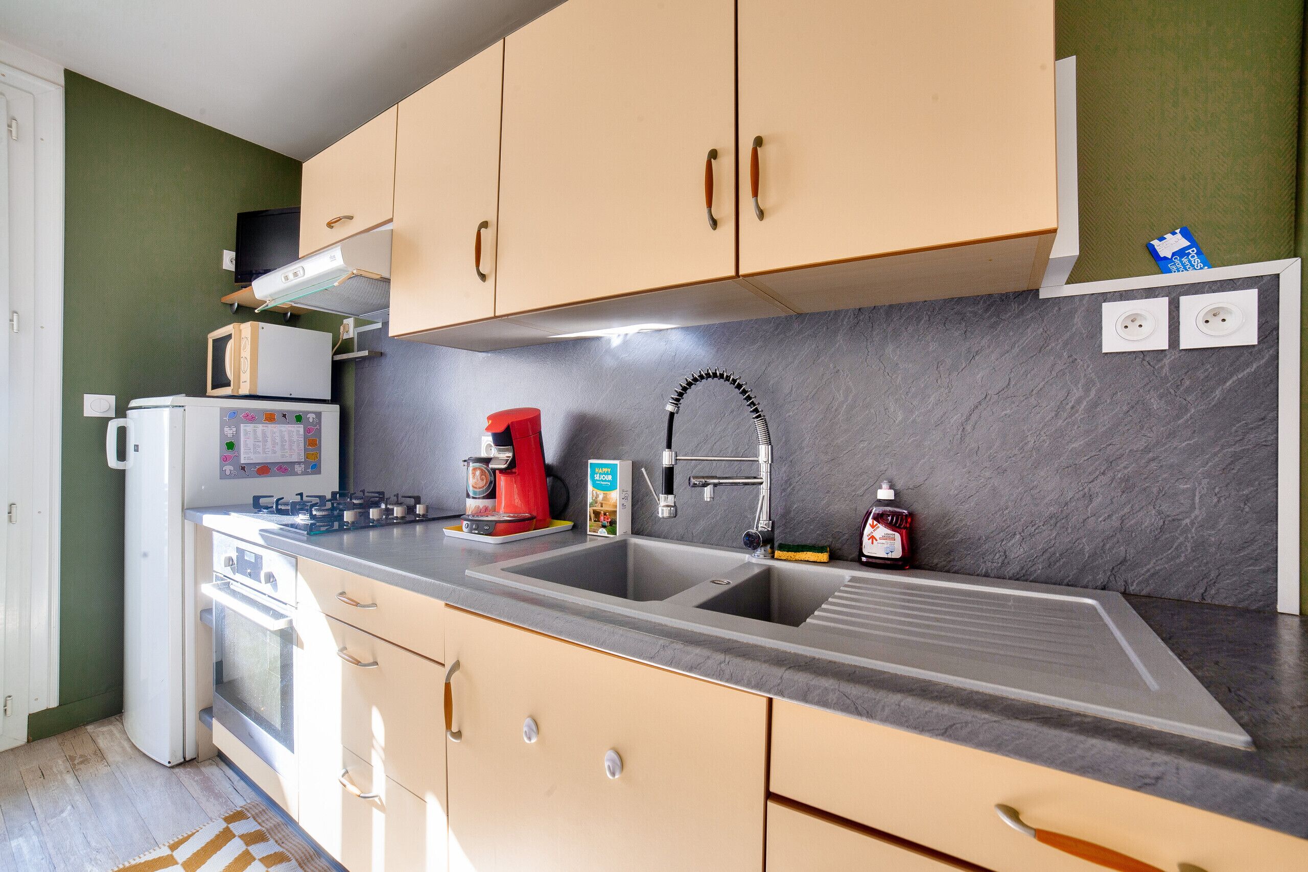 A kitchen with beige cabinets, a double sink, a microwave, a coffee maker, and a refrigerator.