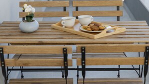 A wooden table with a tray holding two white cups, a small potted orchid, and a plate of cookies.