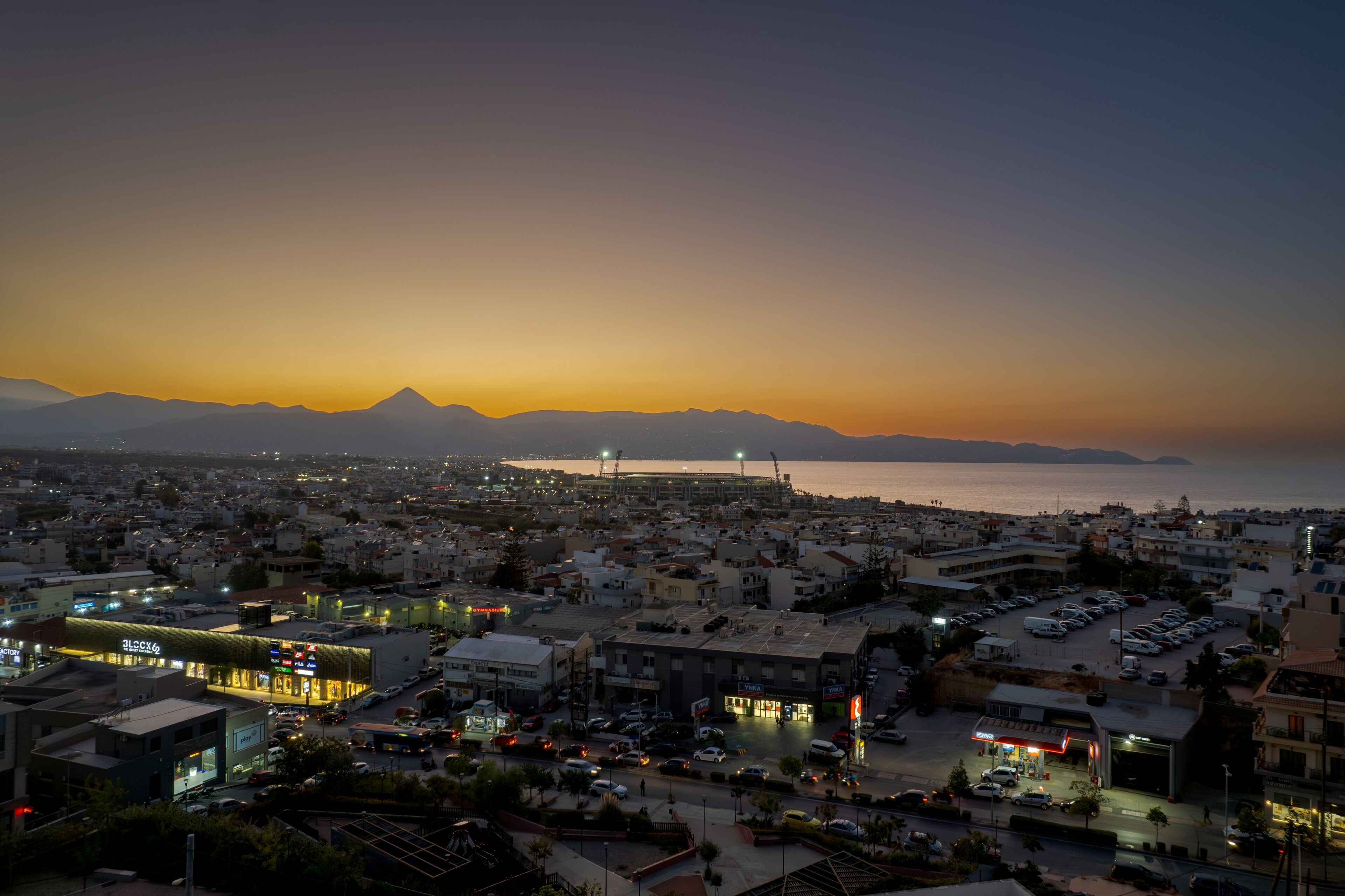 Une vue sur une ville au crépuscule, avec la mer et les montagnes en arrière-plan.