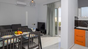 A modern living room with a sofa, dining table, and TV. There is a balcony with a view.