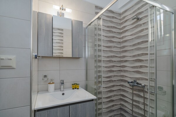 A modern bathroom with a glass shower enclosure, a white sink, and a mirror above it.