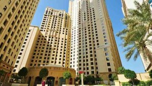 A high-rise building with multiple floors, a central entrance, and surrounding palm trees.