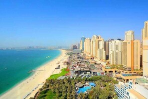 A coastal cityscape with high-rise buildings, a beach, and a resort area with pools and greenery.