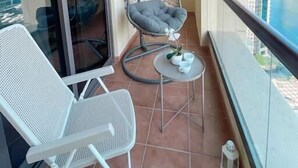 A balcony with a white mesh chair, a hanging chair, and a small table with cups and a plant.