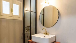 Un baño con lavamanos blanco, un espejo redondo, tocador de madera, inodoro y piso con diseño.