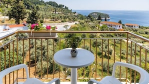 A balcony with a round table and two chairs, overlooking a coastal landscape with houses and greenery. - Skopelos Seaview Suite - Athena Summer Nest (Stafylos)