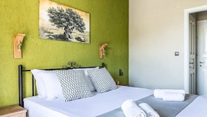 A neatly made bed with white linens and patterned pillows, a green textured wall, and a painting of a tree. - Skopelos Seaview Suite - Athena Summer Nest (Stafylos)