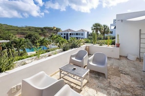 A terrace with a table and chairs, a pool, and a view of a modern house.