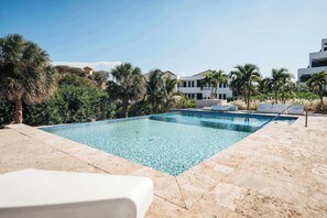 A clear swimming pool with lounge chairs and palm trees, surrounded by modern buildings.