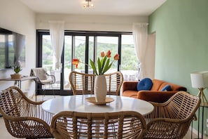 A dining area with wicker furniture, a white table, and a vase with flowers.