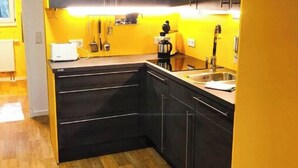 Une cuisine avec des meubles de couleur noire, un plancher en bois et un mur d’accent jaune.
