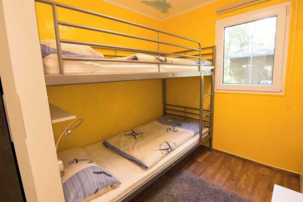 Een slaapkamer met een stapelbed, een raam, houten vloeren en een klein plankje.