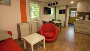 A compact living space with a kitchenette, a dining area, and a red chair. - Meiks Ostsee-Hütten - Holiday home 5 (Dranske)