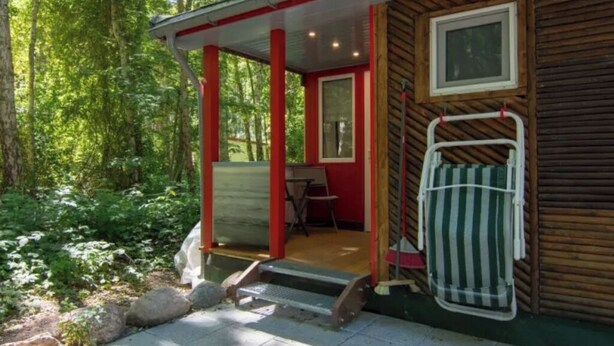 A cabin with a wooden exterior, a porch with red accents, and a window. - Meiks Ostsee-Hütten - Holiday home 5 (Dranske)