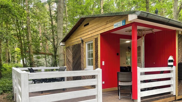 Ein kleines Holzhaus mit roter Fassade, einem weißen Zaun und einer Veranda mit Treppe zum Eingang.