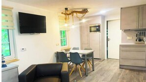 Ein modernes Wohnzimmer mit einer schwarzen Couch, einer Essecke mit Tisch und Stühlen, einer Küche mit Schränken und einer Mikrowelle sowie einem an der Wand montierten Fernseher.