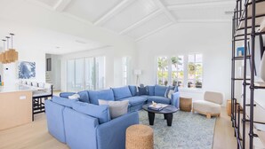 Un salón amplio con un sofá seccional azul grande, una mesa de centro y un comedor con mesa y sillas blancas.