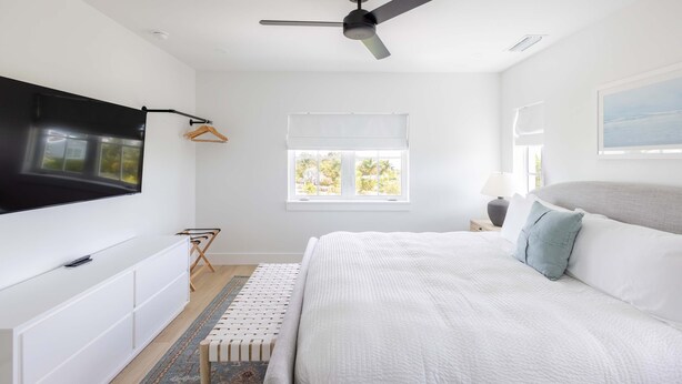 A bedroom with a bed, a TV mounted on the wall, a ceiling fan, and a window with blinds. - Palmgale Estate at Lunara Bay (Key West)