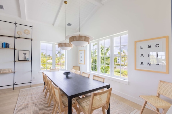 A spacious dining area with a long table, multiple chairs, and large windows offering a view of the outdoors.