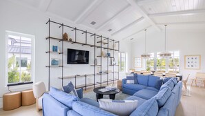 A modern living room with a sectional sofa, a mounted TV, and a black metal shelving unit. - Palmgale Estate at Lunara Bay (Key West)