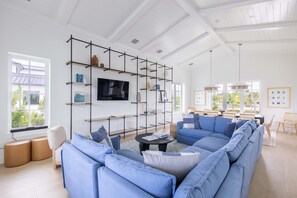 A modern living room with a sectional sofa, a mounted TV, and a black metal shelving unit. - Palmgale Estate at Lunara Bay (Key West)