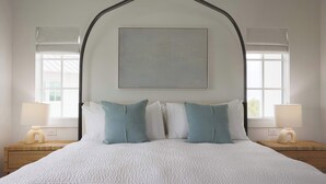 A neatly made bed with white bedding and two pillows, a bedside table with a lamp, and a window with a view. - Floralee House at Lunara Bay (Key West)