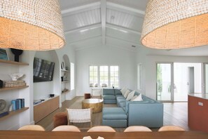 A spacious living room with a sectional sofa, a coffee table, and a TV mounted on the wall. There are two large wicker lamps hanging from the ceiling, and a sliding glass door leading to an outdoor area. - Floralee House at Lunara Bay (Key West)