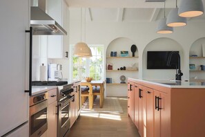 A modern kitchen with stainless steel appliances, a wooden dining table, and pendant lighting.