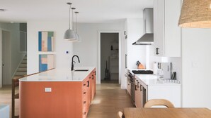 A modern kitchen with a central island, white cabinetry, and a wooden dining table.