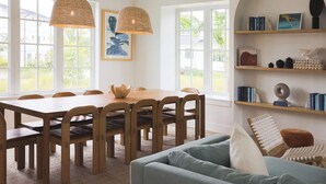 A dining area with a wooden table and chairs, a blue sofa, and a bookshelf with books and decorative items. - Floralee House at Lunara Bay (Key West)