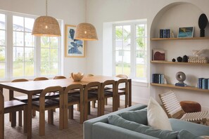 A dining area with a wooden table and chairs, a blue sofa, and a bookshelf with books and decorative items. - Floralee House at Lunara Bay (Key West)