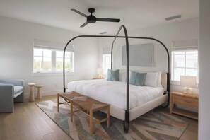 A bedroom with a four-poster bed, a ceiling fan, two bedside tables with lamps, a bench, and a large window.