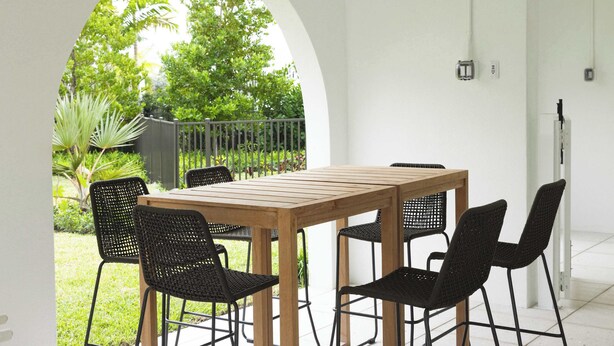 A patio with a wooden table and black chairs, surrounded by white walls and an archway.