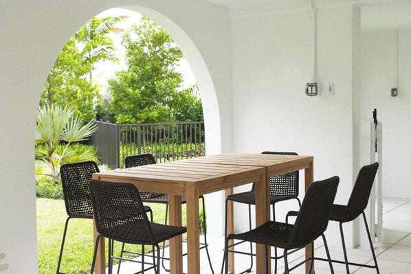 A patio with a wooden table and black chairs, surrounded by white walls and an archway.