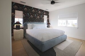 Une chambre à coucher comprenant un lit, deux tables de chevet, une fenêtre avec des stores et un ventilateur de plafond.