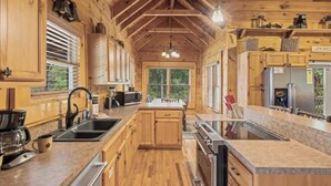 Una cocina estilo cabaña de madera con una isla central, armarios de madera y un ventanal con vistas al exterior.
