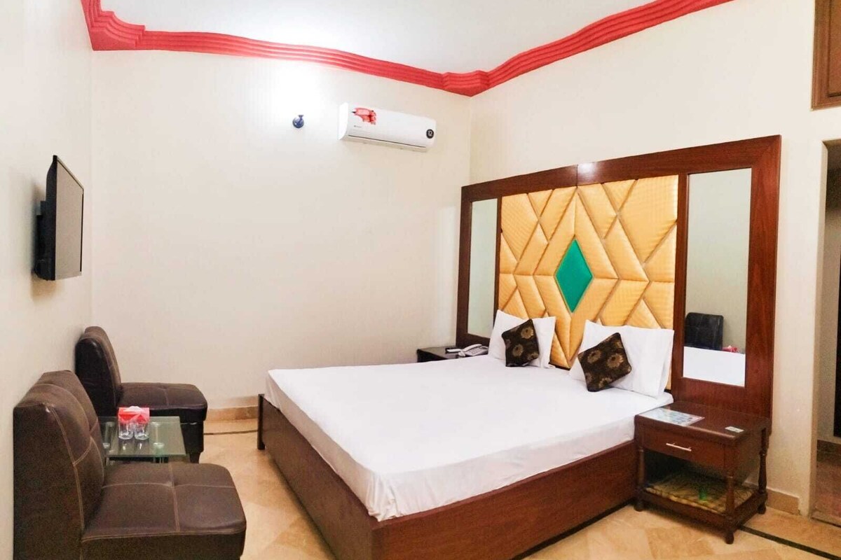 Une chambre d’hôtel avec un grand lit, une tête de lit en bois, un téléviseur à écran plat, une petite table avec deux verres et un canapé marron.