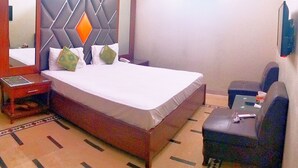 A hotel room with a bed, a bedside table, a chair, a mirror, and a TV. - Hotel Subhan Palace 2 (Karachi)