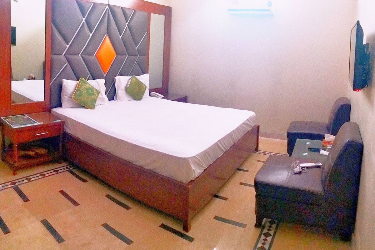 Una habitación de hotel con una cama, una mesita de noche, una silla, un espejo y un televisor.