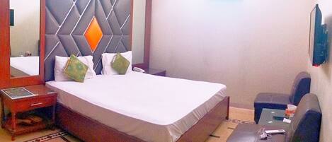 A hotel room with a bed, a bedside table, a chair, a mirror, and a TV.