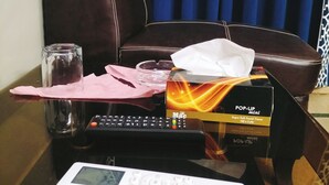 A room with a brown leather chair, a small table with a remote control, a tissue box, a glass, and a pink napkin. - Hotel Subhan Palace 2 (Karachi)