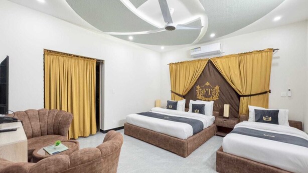 A hotel room with two beds, a sofa, a TV, and an air conditioning unit. - Hotel Subhan Palace 2 (Karachi)