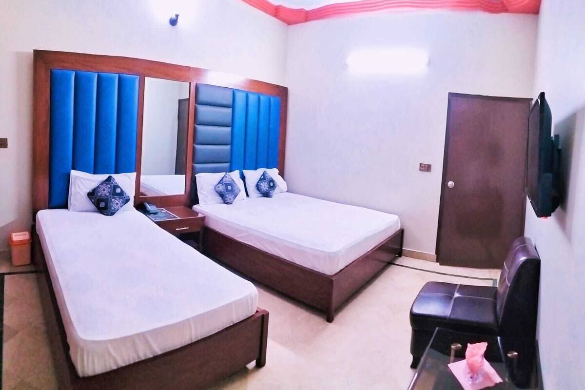 Habitación de hotel con dos camas individuales, cabecera de madera, televisor montado en la pared y escritorio con silla.