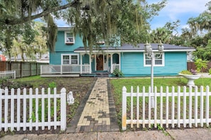 A turquoise house with a white picket fence, a paved pathway, and a porch with a railing.
