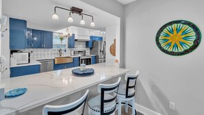 A modern kitchen with blue cabinets, a white island, and a colorful wall decoration. - Relaxing Home Near St. Augustine Attractions 4 Bedroom Residence (St. Augustine)