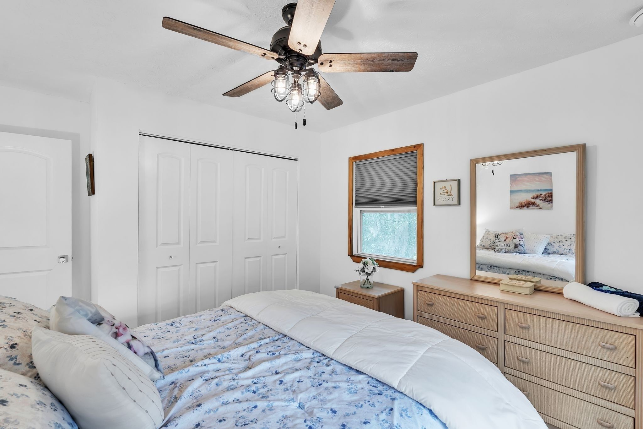 Ein Schlafzimmer mit einem Bett, einem Deckenventilator, einem Schminktisch, einem Spiegel und einem Fenster mit Jalousien.